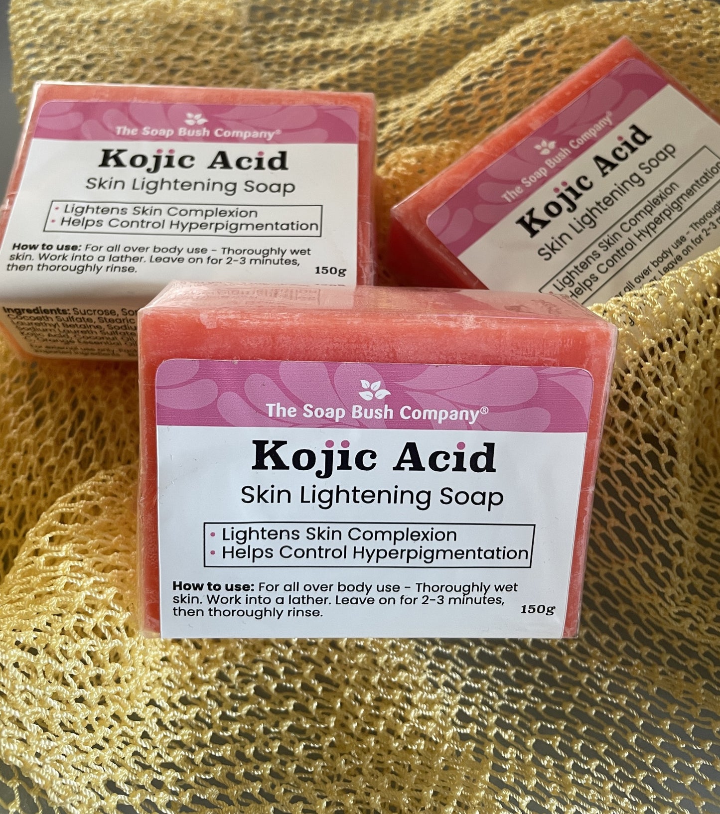 Three pink Kojic Acid skin lightening soaps by The Soap Bush Company, arranged on a textured AFRICAN EXFOLIATING cloth for proper exfoliation